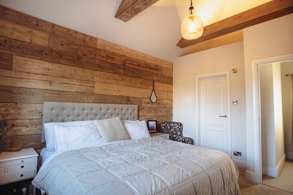 Bedroom with large bed, oak beams and wooden feature wall