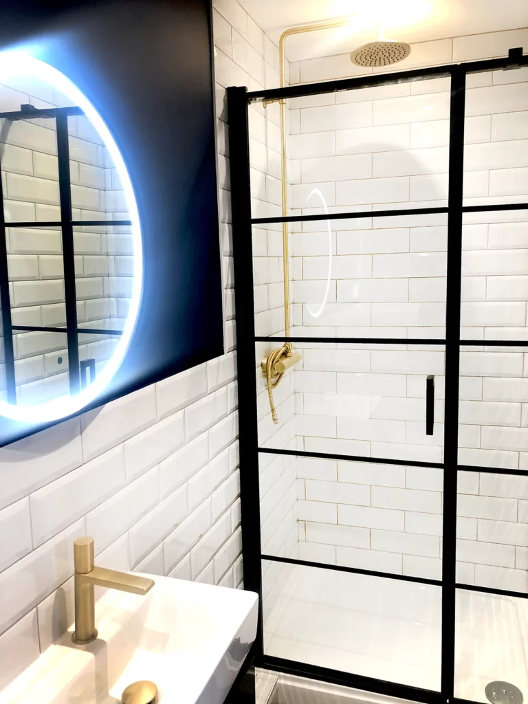 Bathroom with white subway tiles, black shower screen and brushed gold taps