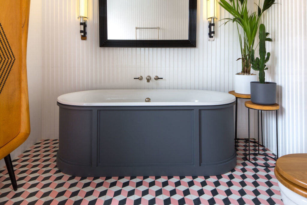 Black panelled freestanding bath with pink and white geometric floor tiles